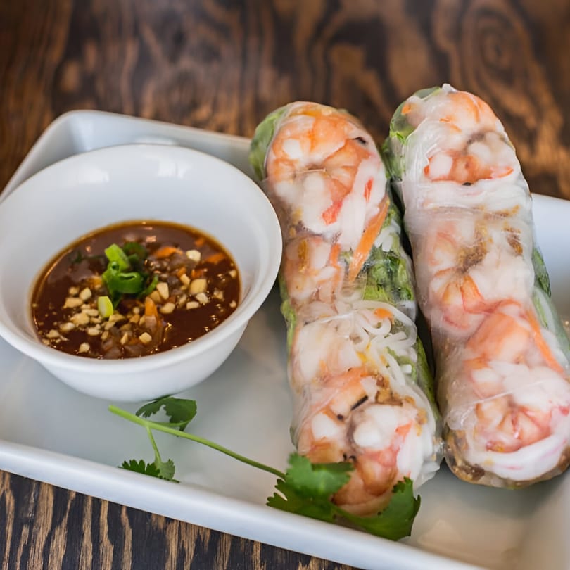 Two Vietnamese spring rolls with shrimp and vegetables, served with a peanut dipping sauce.