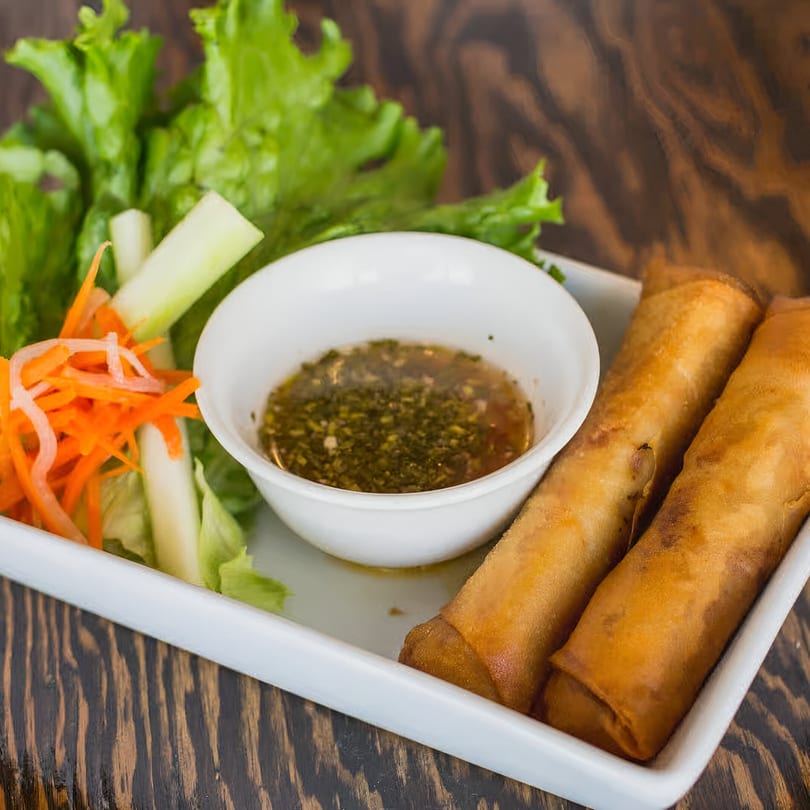 Two crispy Vietnamese spring rolls with fresh lettuce, shredded carrots, and a dipping sauce.