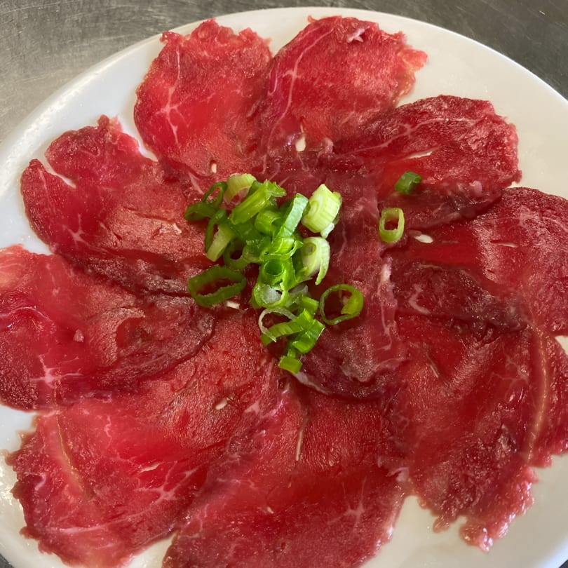 Thinly sliced raw beef, garnished with chopped green onions, on a white plate.