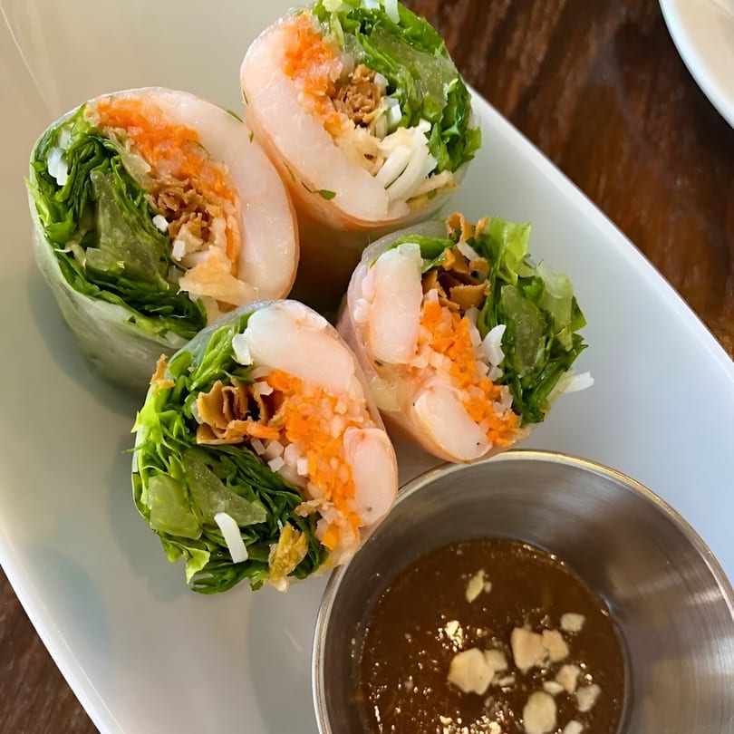 Four Vietnamese spring rolls with shrimp, lettuce, and carrots, served with peanut sauce.