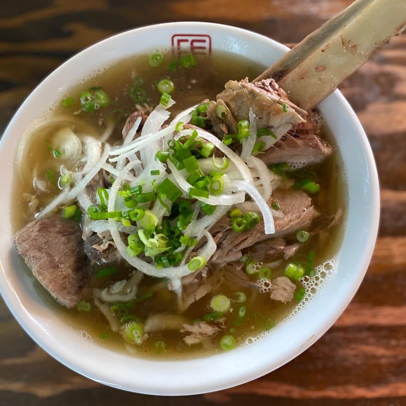Close-up of a bowl of Feu Pho Kitchen's pho with beef, noodles, onions, and a large bone.