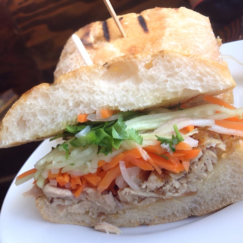 A close-up of a Vietnamese banh mi sandwich filled with meat, pickled carrots, and cilantro.