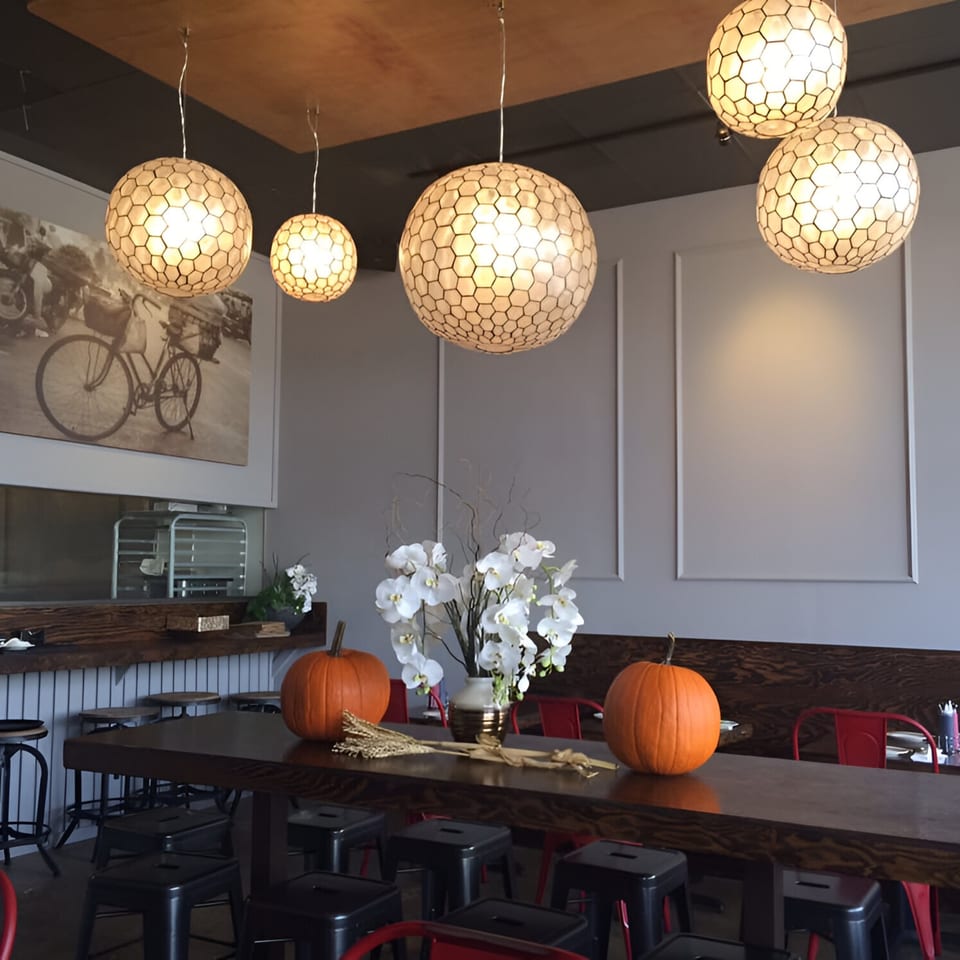 Feu Pho Kitchen dining room with hexagonal pendant lights, a long communal table, and fall decorations.