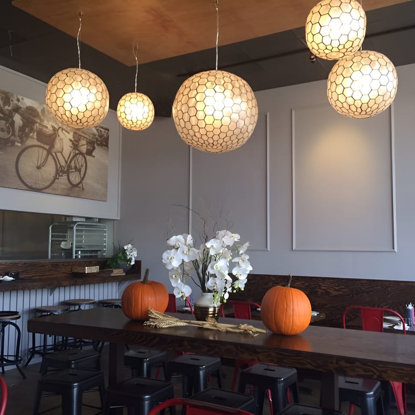 Feu Pho Kitchen dining room with hexagonal pendant lights, a long communal table, and fall decorations.