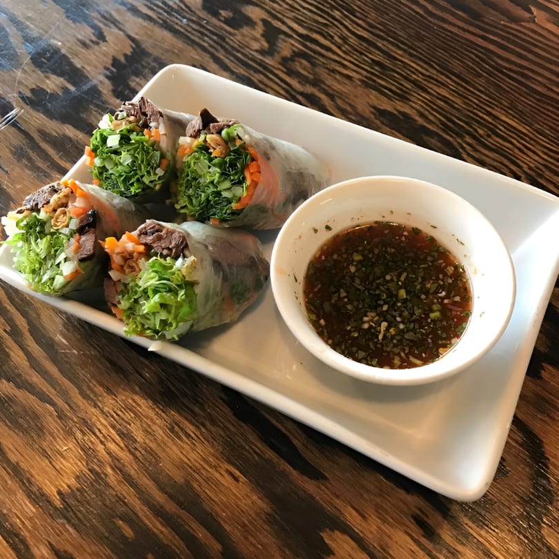 Four Vietnamese spring rolls filled with meat and vegetables, served with a dipping sauce on a white plate.